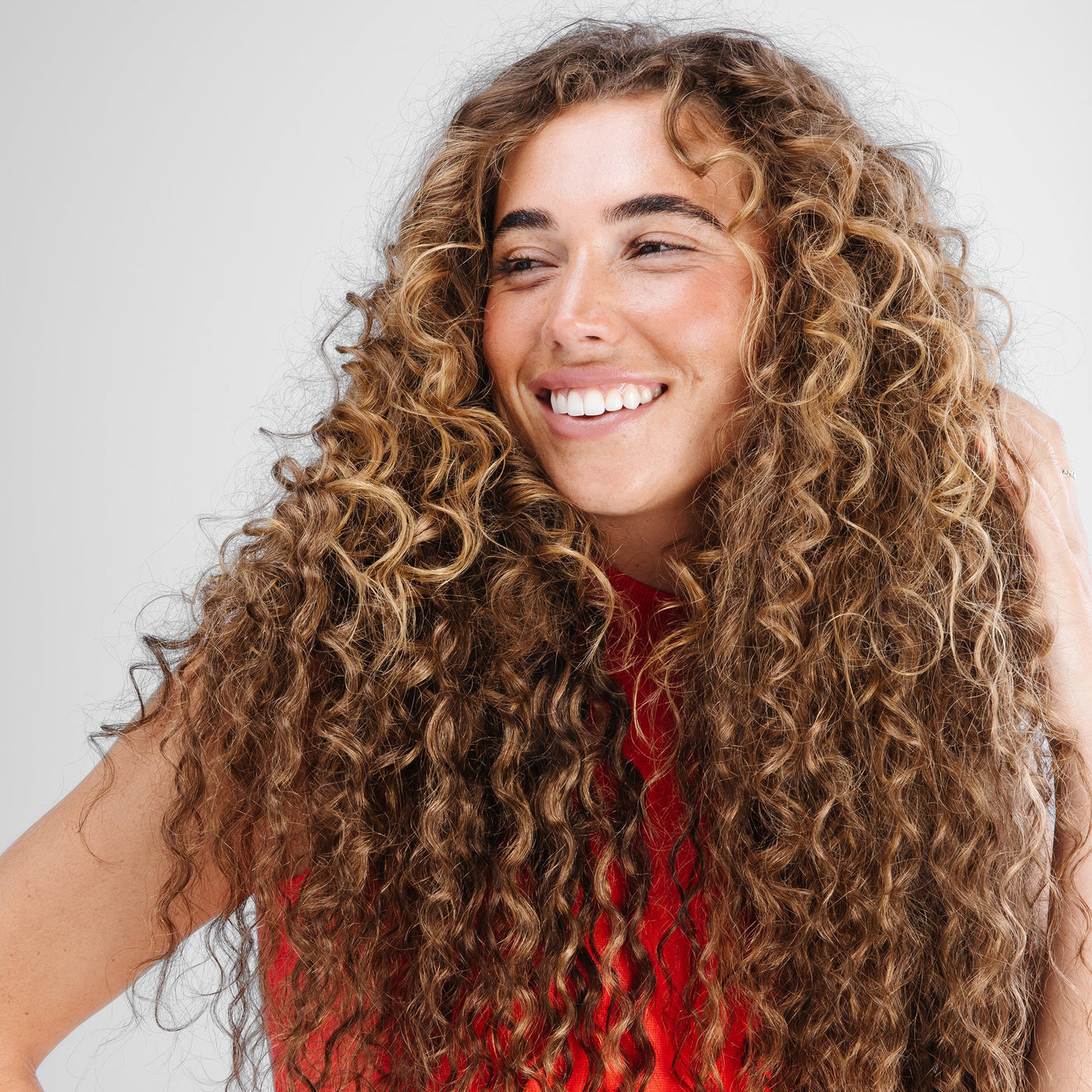 A cheerful woman with curly hair extensions displaying a bright smile.