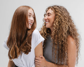 Two women with curly hair extensions, sharing a moment of laughter and joy.