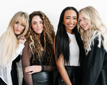 Four women with various hair extensions pose together for a group photo all smiling.